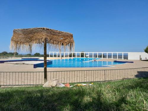 a swimming pool with a straw umbrella next to a fence at Cantinho D'Avó Maria in Zebreira