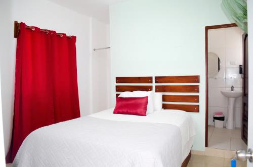 a bedroom with a white bed with a red curtain at Hotel las Nina in Paraíso