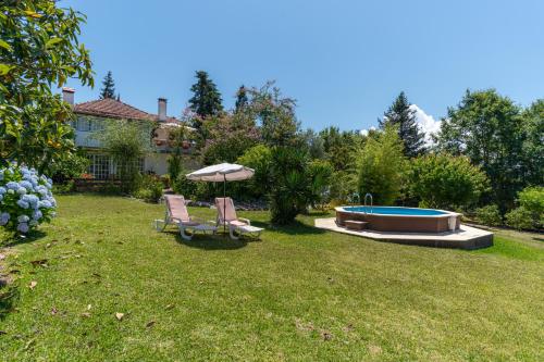 a yard with two chairs and an umbrella and a pool at Atlantic Nest Poiares in Vila Nova de Poiares
