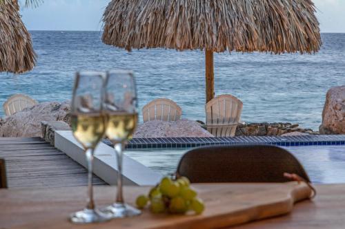 two glasses of wine sitting on a table near the ocean at PM78 Boutique Apartments in Willemstad