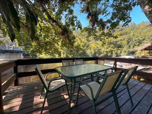 a green table and chairs on a deck with a view at Casa Una à Beira Rio - Barra do Una - 450m da praia in São Sebastião
