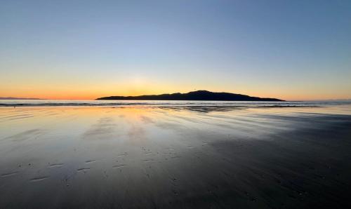 a view of a beach with the sun setting at Tudor Manor Bed & Breakfast in Paraparaumu Beach
