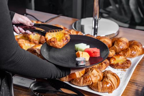 a person holding a plate of food on a table with pastries at Travelodge Hotel Hurstville Sydney in Sydney