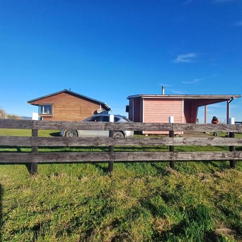 a fence in front of a house and a car at Cabañas MAR BRAVA in Ancud