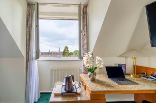 a desk with a laptop on it with a window at PLAZA INN Blankenburg Ditzingen, Sure Hotel Collection in Ditzingen