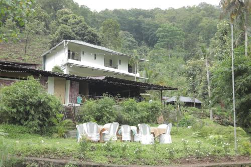 a group of white chairs in front of a house at Pepper and Clove Enclave in Puliyara
