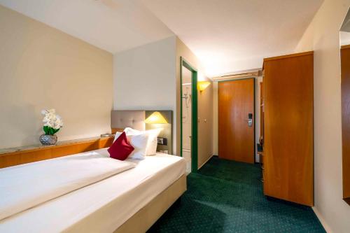 a bedroom with a large white bed with a red pillow at PLAZA INN Blankenburg Ditzingen, Sure Hotel Collection in Ditzingen