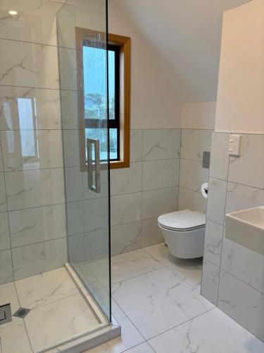 a bathroom with a glass shower and a toilet at Absolute Beachfront Holiday Home With Private Beach Access To Swim Beach Spectacular Sunsets in Paraparaumu