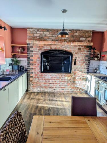 a kitchen with a brick fireplace and a wooden table at The Cob House. in Ifton Heath