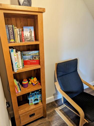 a chair next to a book shelf with books at The Cob House. in Ifton Heath