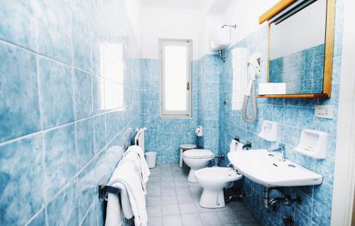 a blue tiled bathroom with two toilets and a sink at Hotel San Giuan in Alghero