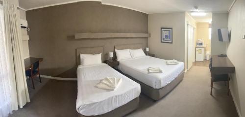 a bedroom with two beds with white sheets and a desk at Mid City Plantation Motel in Mildura