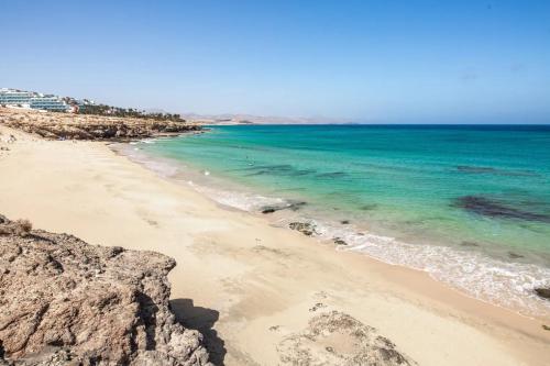 a beach with the blue water and rocks at Solymar Jasmin A8 in Costa Calma