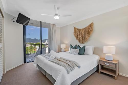 a white bedroom with a bed and a balcony at Esplanade Escape in Cairns