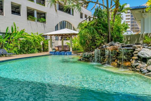a swimming pool with a waterfall in front of a building at Esplanade Escape in Cairns