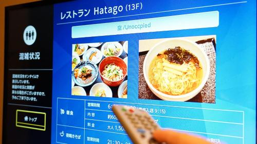 a person holding a remote control in front of a menu at Dormy Inn Kumamoto Natural Hot Spring in Kumamoto