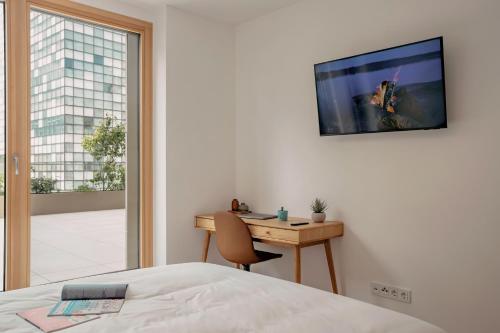 a bedroom with a bed and a desk with a television on the wall at Media Bay Apartments in Kirchberg by Rentaroo in Luxembourg