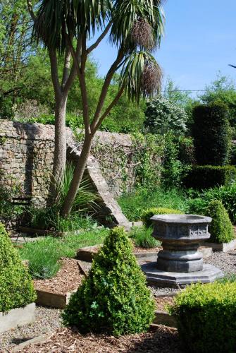 a garden with a tree and a stone wall at Cottage de charme & jardin fabuleux à 800m de la mer - Maison Melchior in Flamanville