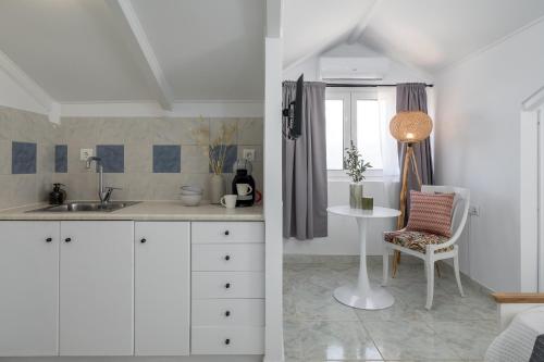 a kitchen with white cabinets and a table and a chair at Eraora Lofts & Apartments Kefalonia in Lakithra