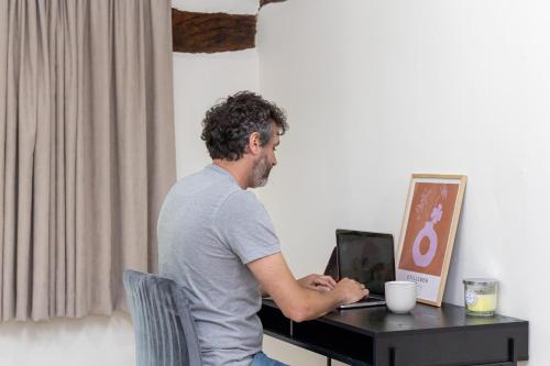 a man sitting at a desk with a laptop computer at River Fishing I Hot tub I Games Room I PetFriendly in Rainow