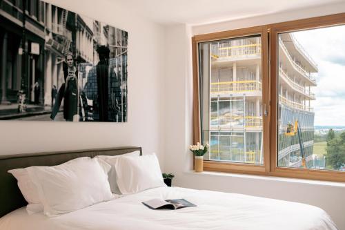 a bed with a book on it next to a window at Media Bay Apartments in Kirchberg by Rentaroo in Luxembourg