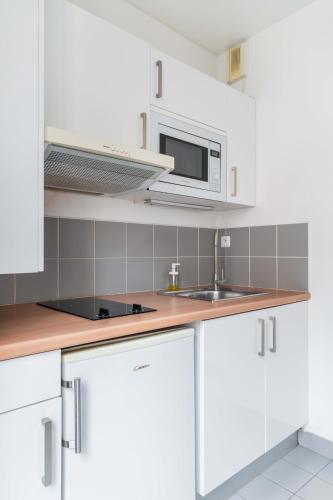 une cuisine avec des armoires blanches et un micro-ondes dans l'établissement 204 - Charmant studio jardins des plantes -Paris 5 - FLAT-GUEST, à Paris