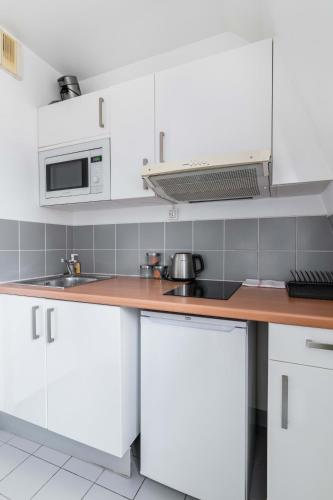 une cuisine avec des armoires blanches et un micro-ondes dans l'établissement 505- Charmant studio jardins des plantes -Paris 5 - FLAT-GUEST, à Paris