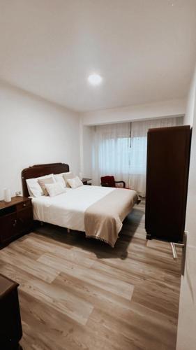 a bedroom with a white bed and a wooden floor at Piso BOIRO PLAYA Robustiano in Boiro