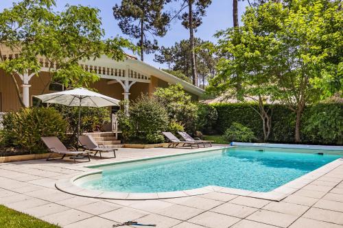- une piscine avec des chaises et un parasol à côté d'une maison dans l'établissement Villa familiale avec piscine dans la pinède à 4min de l'océan-AG13, à Lacanau