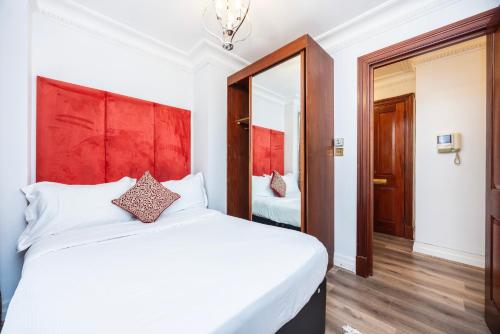 a bedroom with a large white bed with a red headboard at CARLTON COURT - MAYFAIR in London