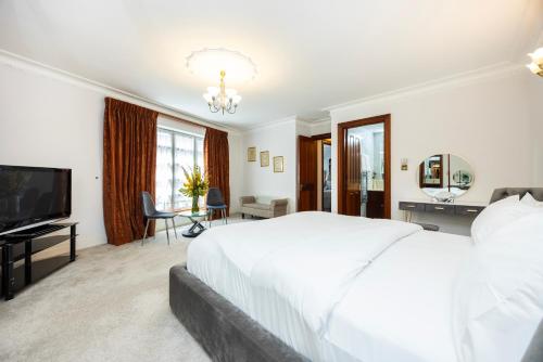 a white bedroom with a large bed and a flat screen tv at CARLTON COURT - MAYFAIR in London