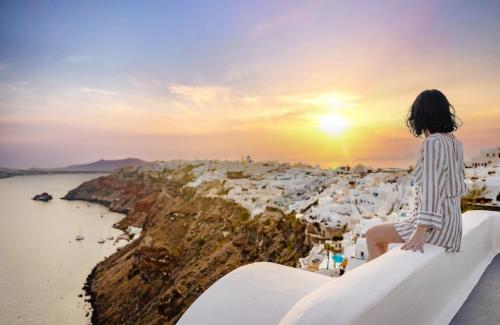 a woman sitting on the edge of a cliff watching the sunset at IKIES Santorini in Oia