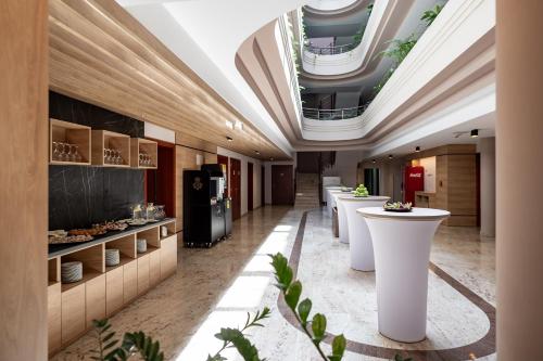 a lobby with a row of white tables and ceilings at Airport Hotel Budapest in Vecsés