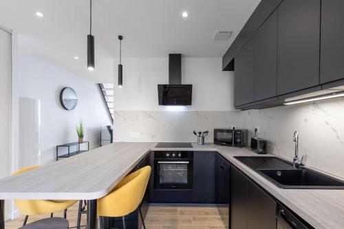 une cuisine avec des armoires noires et des chaises jaunes dans l'établissement T3 neuf avec extérieur, à Saint-Georges-de-Reneins