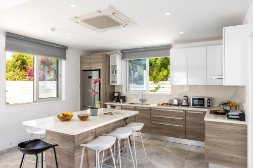 a kitchen with white cabinets and a island with bar stools at Fig Tree Bay Residences 1 Lantiana Villa in Protaras