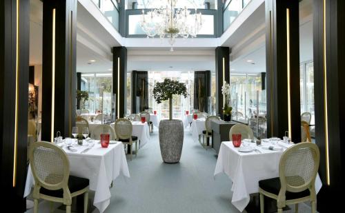 a restaurant with white tables and chairs and a chandelier at Mondorf Parc Hotel & Spa in Mondorf-les-Bains