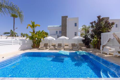 a pool with chairs and umbrellas next to a building at Fig Tree Bay Residences 1 Lantiana Villa in Protaras