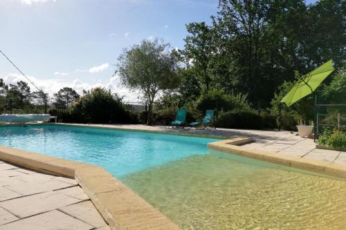 - une piscine avec un parasol vert et des chaises dans l'établissement Le Roqual, à Carsac-Aillac