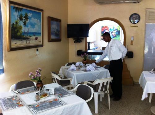 a man standing in a dining room with tables at Hotel Caribe in Santa Cruz de Barahona