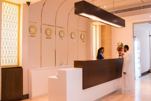 two people standing at a counter in a room with clocks at City Park Hotel Apartments in Muscat