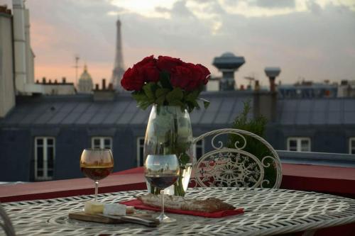 une table avec deux verres de vin et un vase de roses dans l'établissement Amazing Rooftop Odeon Luxembourg, à Paris