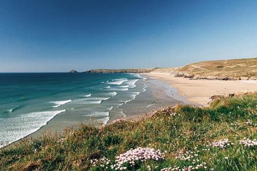 a beach with white flowers and the ocean at Cosy 3 bedroom home, 2 minutes from the beach in Perranporth