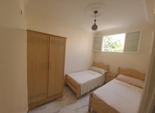 a bedroom with two beds and a cabinet and a window at Luxury Cosy Apartment in Al Hoceima, Morocco in Al Hoceïma