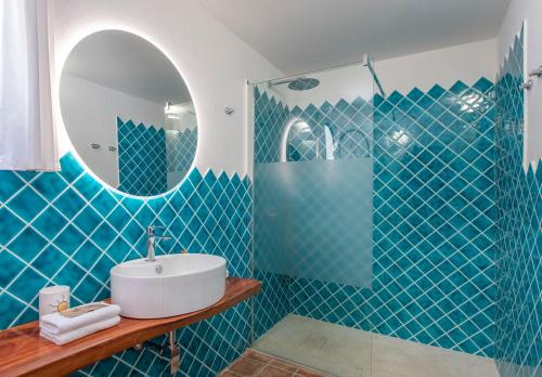 Un baño con azulejos azules, lavabo y espejo. en Villa Eliana sul Mare, en Porto Pino