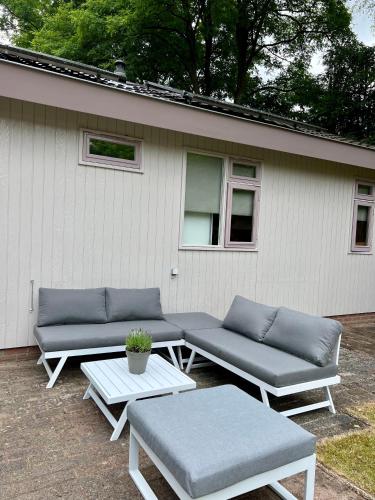 a patio with couches and tables in front of a house at Luxe Boshuisje met Privé Wellness & Jacuzzi op de Veluwe in Ermelo