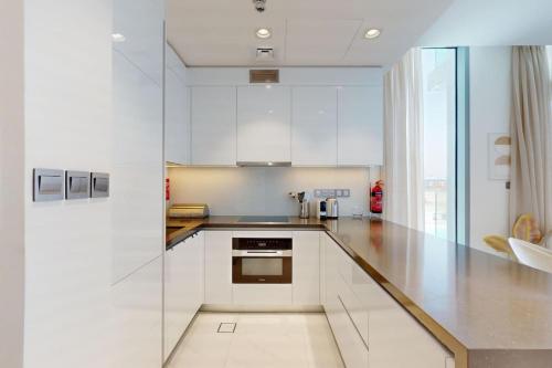 a white kitchen with white cabinets and a sink at Vacationer Holiday Homes I Waterfront 1 Bedroom I Stunning Lagoon View I District One in Dubai