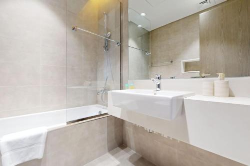 a white bathroom with a sink and a shower at Vacationer Holiday Homes I Waterfront 1 Bedroom I Stunning Lagoon View I District One in Dubai