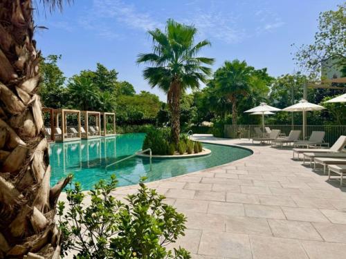 a swimming pool with chairs and a palm tree at Vacationer Holiday Homes I Waterfront 1 Bedroom I Stunning Lagoon View I District One in Dubai