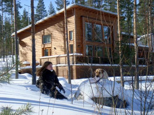 a woman and a dog in the snow in front of a log cabin at PielisLinna in Kolinkylä