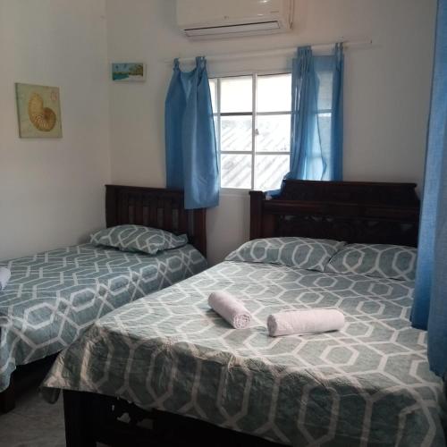 two beds in a bedroom with blue curtains at Right Lang Deh Soh in San Andrés